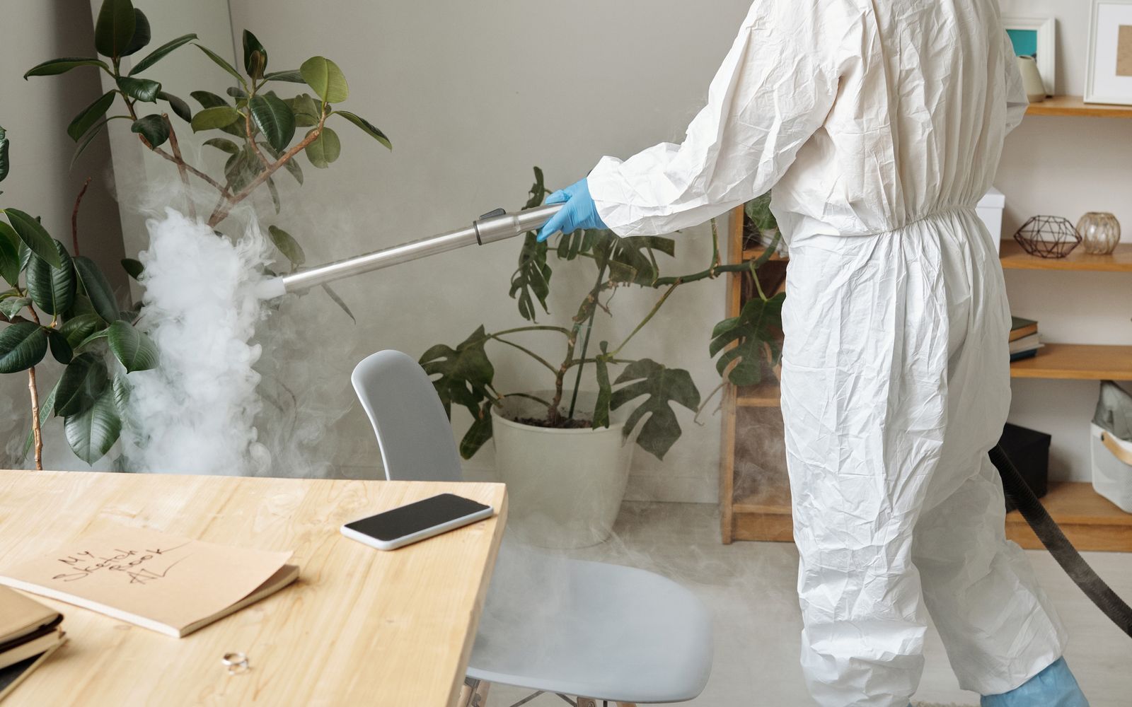 Technician in protective gear applying disinfectant treatment in a commercial space