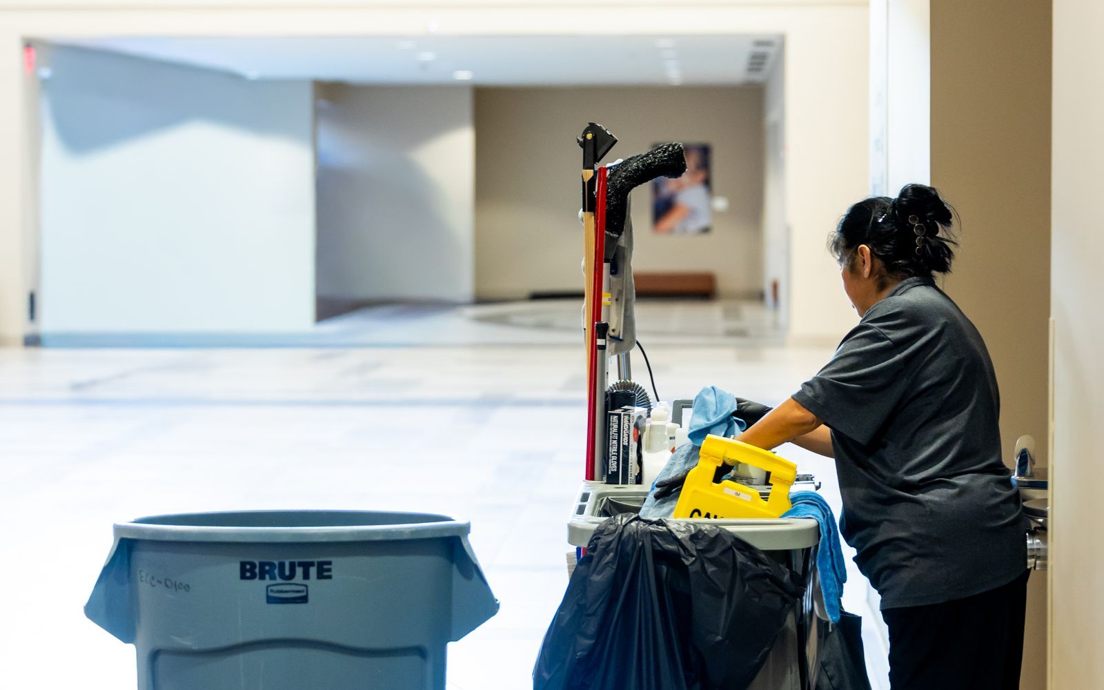Janitorial worker moving a supply cart through a building hallway
